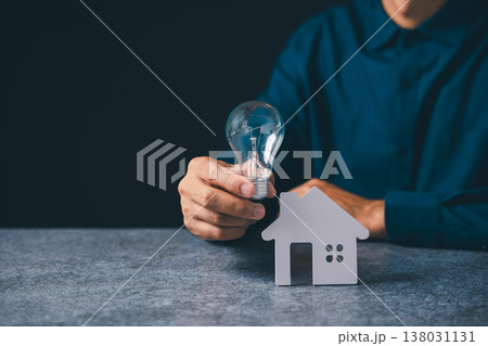 Hand holding light bulb near house model for real estate innovation, home energy idea representing property mortgage savings, creative electricity knowledge regarding lightbulb Hand holding light bulb near house model for real estate innovation, home energy idea representing property mortgage savings, creative electricity knowledge regarding lightbulb 138031131
