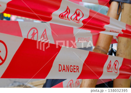 Red and white danger warning barrier tape with hazard symbols on construction site 138032395