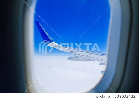 Airplane wing and white clouds seen through oval passenger window porthole during daytime flight travel Airplane wing and white clouds seen through oval passenger window porthole during daytime flight travel 138032432