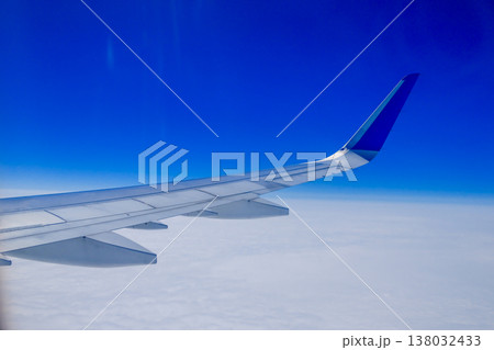 Airplane wing over white clouds with vivid blue sky horizon view from passenger window during flight Airplane wing over white clouds with vivid blue sky horizon view from passenger window during flight 138032433