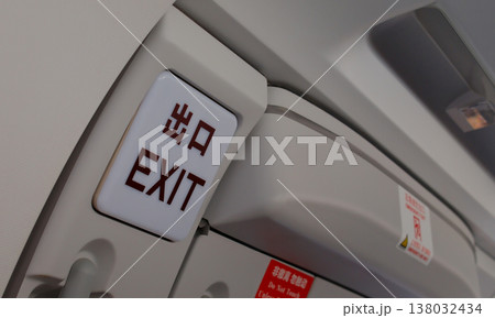 EXIT emergency sign on airplane cabin ceiling panel above passenger seat in aircraft interior 138032434