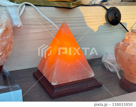 Himalayan salt lamp pyramid glowing warm light on wooden base. Interior decor, wellness concept, ambient lighting 138033850