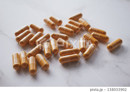 Premium flatlay with bright curcumin capsules scattered on white marble, contrasting vibrant turmeric hues with cool stone texture for a clean wellness aesthetic 138033902