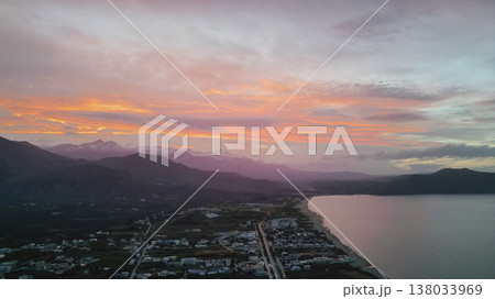 Aerial panoramic view of Crete coastline at twilight with colorful pre-sunset sky, valley with fields and villages, mountain ridge, and reflective sea bay 138033969