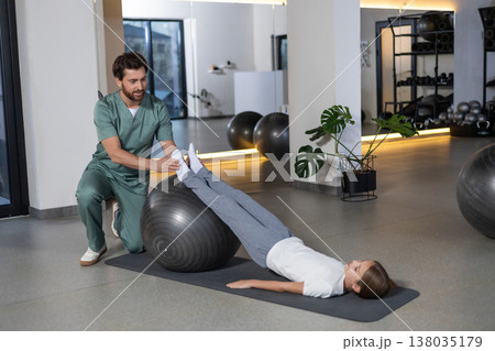 Physiotherapist assisting child with fitness ball training Physiotherapist assisting child with fitness ball training 138035179