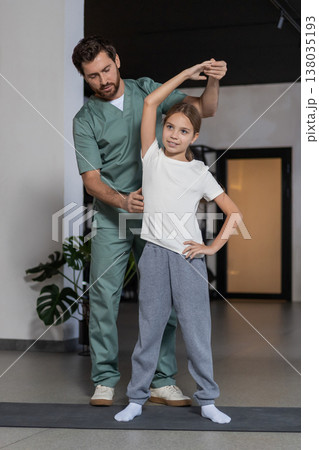 Specialist assisting girl with standing side bends 138035193