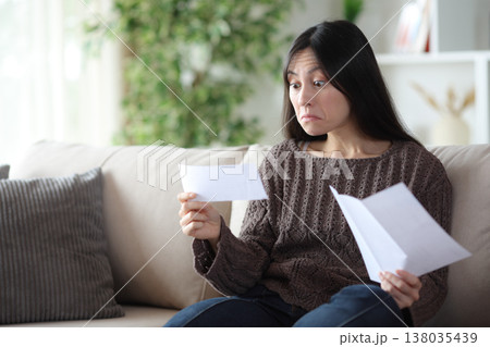 Perplexed asian woman reading paper letter at home 138035439
