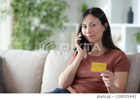 Satisfied asian customer making phone call holding card 138035442