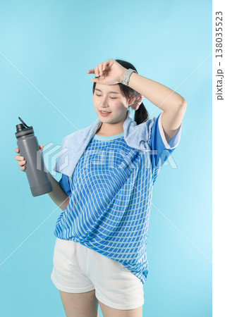 Tired sweat sport woman teen holding a water bottle and a towel standing rest isolated in studio Tired sweat sport woman teen holding a water bottle and a towel standing rest isolated in studio 138035523