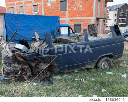 Abandoned wrecked van body standing on grass beside unfinished brick housing block. Vehicle decay, urban neglect, scrapyard condition, derelict transport, redevelopment contrast, post industrial 138036043