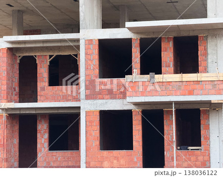 Brick wall sections with window openings in unfinished apartment building facade. Masonry work, construction progress, residential development, material layering, structural assembly, urban housing 138036122