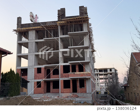 Unfinished residential building with concrete frame and brick walls at construction site. Urban development, real estate investment, housing expansion, civil engineering process, suburban growth Unfinished residential building with concrete frame and brick walls at construction site. Urban development, real estate investment, housing expansion, civil engineering process, suburban growth 138036124