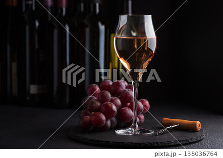 Glasses of sparkling rose wine with corkscrew and bunch of grapes on dark slate surface against bottles in background Glasses of sparkling rose wine with corkscrew and bunch of grapes on dark slate surface against bottles in background 138036764