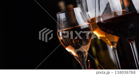 Close-up three glasses of red, white and sparkling rose wine with bunch of grapes on dark slate surface against bottles in background 138036768