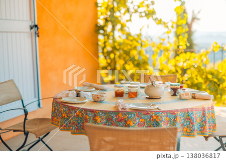 Idyllic morning breakfast with table and chairs, sunlight, Mediterranean outdoor terrace, grape vines, serene atmosphere Idyllic morning breakfast with table and chairs, sunlight, Mediterranean outdoor terrace, grape vines, serene atmosphere 138036817