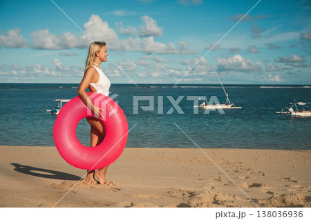 Woman stands on sandy beach holding a float ring 138036936