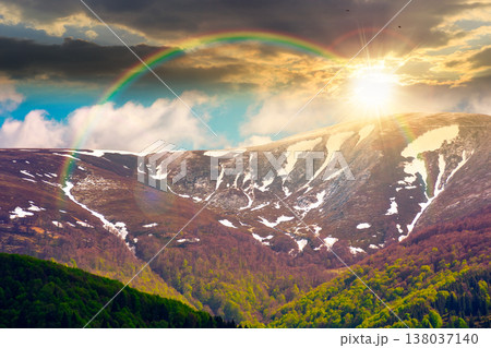sunset over nature image of ridge with snow capped tops in spring landscape. mountain background wallpaper. greenery scenery with forested slopes under rainbow and sky with clouds 138037140