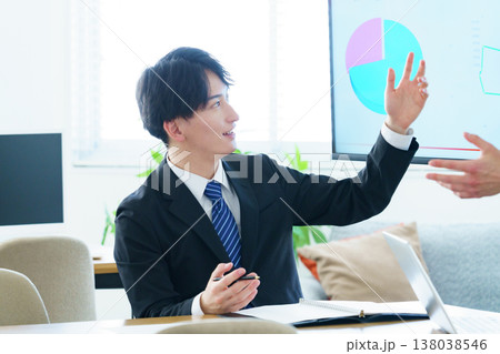 オフィスでディスプレイに映ったグラフを説明しながらプレゼンをする若い男性 オフィスでディスプレイに映ったグラフを説明しながらプレゼンをする若い男性 138038546
