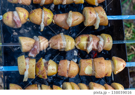 Potatoes with lard are grilled on a skewer over open flames, creating a rustic and flavorful outdoor meal. 138039016