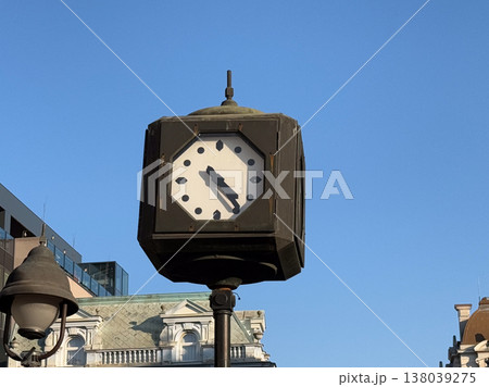 Historic street clock on a metal post rising above classical city architecture under a cloudless sky. Urban timekeeping, heritage streetscape, and old town landmark detail in bright daylight 138039275