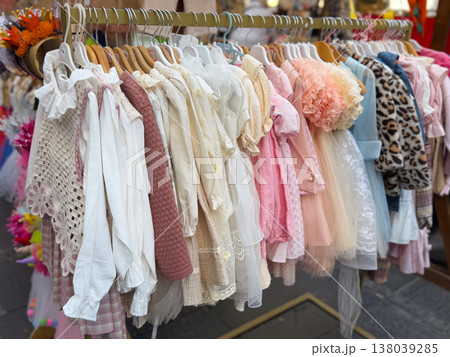 Boutique rack with elegant girls clothing in lace, tulle, and pastel fabrics at a market. Children fashion retail, occasion dressing, curated assortment, and premium textile presentation for festive Boutique rack with elegant girls clothing in lace, tulle, and pastel fabrics at a market. Children fashion retail, occasion dressing, curated assortment, and premium textile presentation for festive 138039285