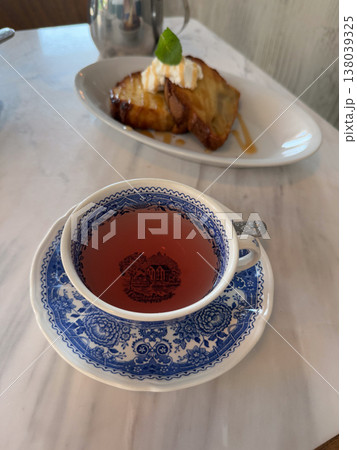 Herbal tea in a blue patterned cup with pastry and cream on a marble table. Cafe dessert pause, afternoon refreshment, sweet serving, and tabletop hospitality detail in soft daylight 138039325