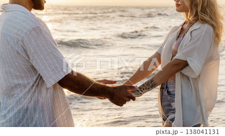 Couple holding hands at sunset by the ocean shoreline Couple holding hands at sunset by the ocean shoreline 138041131