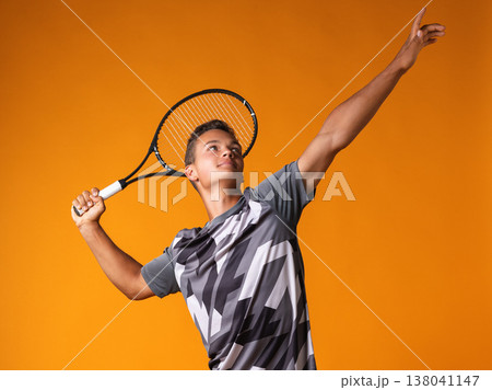 Young player practices tennis serve in studio with bright orange background Young player practices tennis serve in studio with bright orange background 138041147