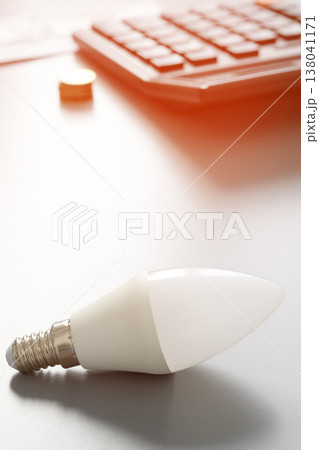 Light bulb rests on a desk next to a keyboard and coins during the daytime 138041171