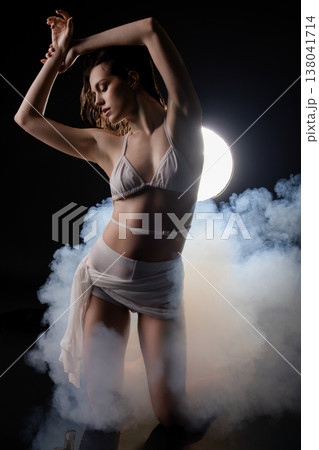 Graceful woman with wet hair dancing in smoke with dramatic backlight. 138041714