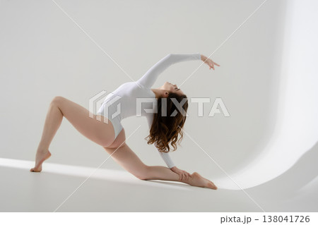 Flexible woman in a white leotard performing a graceful, dynamic stretch on a clean white background. 138041726