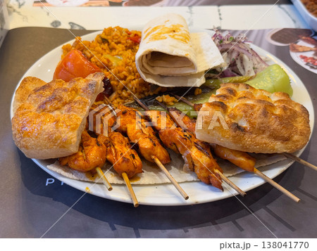 Grilled chicken skewers with bulgur pilaf, lavash, pide, onion salad and roasted vegetables on plate. Turkish restaurant assortment, mixed lunch serving, protein rich meal, regional menu choice Grilled chicken skewers with bulgur pilaf, lavash, pide, onion salad and roasted vegetables on plate. Turkish restaurant assortment, mixed lunch serving, protein rich meal, regional menu choice 138041770