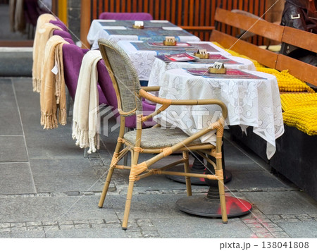 Outdoor cafe seating with wicker chairs and wooden tables along sidewalk partition. Urban hospitality setting, street dining arrangement, small business service, leisure environment, public space 138041808