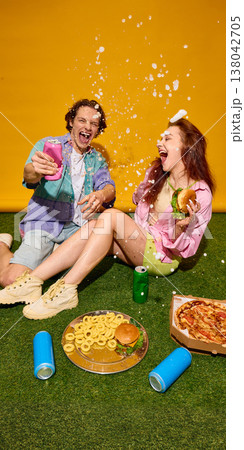 Young couple laughing with splashing drink and fast food on grass bright yellow background. 138042705