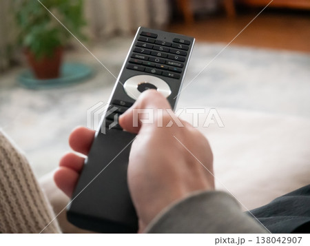 Man hand holding television remote control. Finger pressing button on controller to change channel or volume at home. Entertainment device for multimedia equipment and smart home technology. 138042907