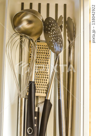Top-down view of essential stainless steel kitchen utensils neatly organized in a white modern kitchen drawer Top-down view of essential stainless steel kitchen utensils neatly organized in a white modern kitchen drawer 138042922