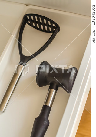 Potato masher and meat tenderizer mallet neatly stored in a clean white kitchen utensil drawer. Home organization. Potato masher and meat tenderizer mallet neatly stored in a clean white kitchen utensil drawer. Home organization. 138042952