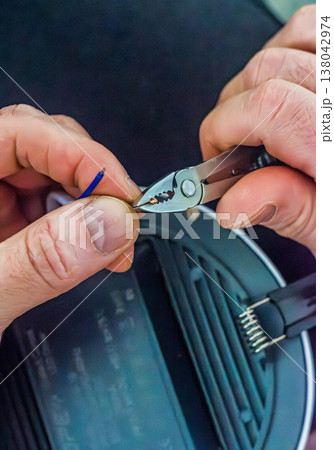 Close-up of an electrician's hands using a wire stripper to prepare a copper wire for an electrical installation or repair. Close-up of an electrician's hands using a wire stripper to prepare a copper wire for an electrical installation or repair. 138042974