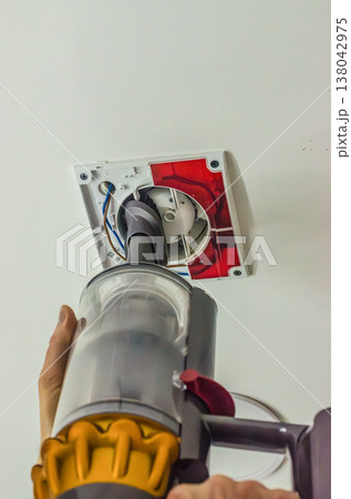 Cleaning a dirty ceiling exhaust fan with a modern handheld vacuum cleaner. Home maintenance and hygiene concept. Cleaning a dirty ceiling exhaust fan with a modern handheld vacuum cleaner. Home maintenance and hygiene concept. 138042975