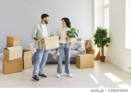 Happy couple moving into new home, carrying boxes and houseplants together Happy couple moving into new home, carrying boxes and houseplants together 138043000