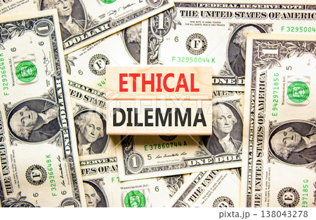 Ethical dilemma words symbol. Concept words Ethical dilemma on beautiful wooden blocks. Beautiful dollar bills background. Dollar bills. Business and Ethical dilemma words concept. Copy space. 138043278