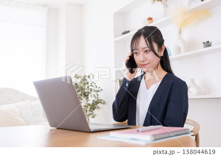 パソコンを見ながらスマホで話す20代女性 138044619