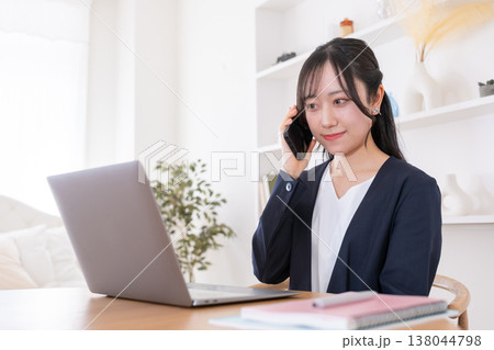パソコンを見ながらスマホで話す20代女性 138044798