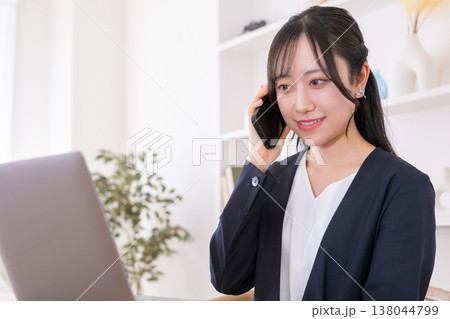 パソコンを見ながらスマホで話す20代女性 138044799
