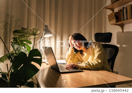 Exhausted woman experiencing burnout and stress while working on her laptop in a dark home office environment Exhausted woman experiencing burnout and stress while working on her laptop in a dark home office environment 138045442