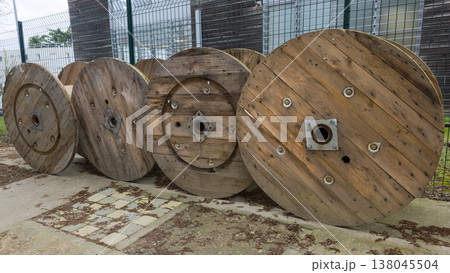 Large wooden cable spools on a construction site. Row of massive empty industrial reels for electrical wire, power cables, and telecommunications infrastructure. Outdoor storage of utility equipment. Large wooden cable spools on a construction site. Row of massive empty industrial reels for electrical wire, power cables, and telecommunications infrastructure. Outdoor storage of utility equipment. 138045504