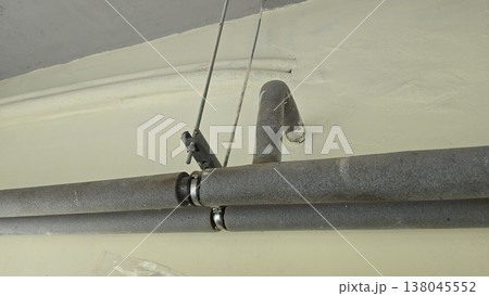 Insulated pipes with gray foam covers are mounted to a ceiling with metal brackets and threaded rods in a utility room. Insulated pipes with gray foam covers are mounted to a ceiling with metal brackets and threaded rods in a utility room. 138045552