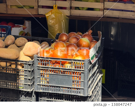 Crates of fresh onions and potatoes displayed at local market stall in daylight. Food retail, agricultural produce, grocery shopping, natural ingredients, everyday market supply 138047247