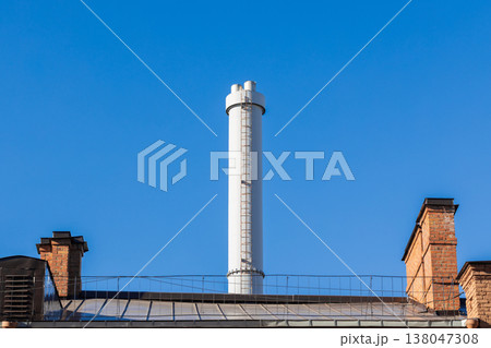 A tall industrial chimney stack rises behind an old house 138047308