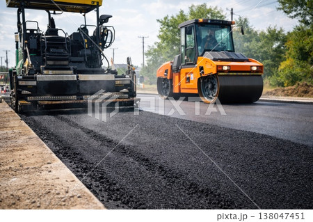 Asphalt paving machine and road roller working on new roadway surface 138047451